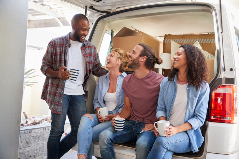 Freunde helfen bei einem Umzug und sitzen lachend auf einem beladenen Transporter