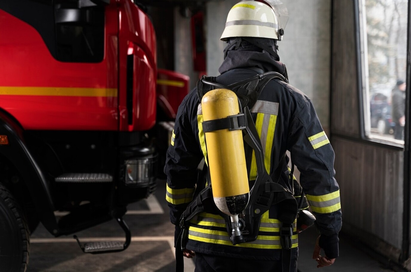 Ein Feuerwehrmann im Anzug von hinten neben einem Feuerwehrwagen.