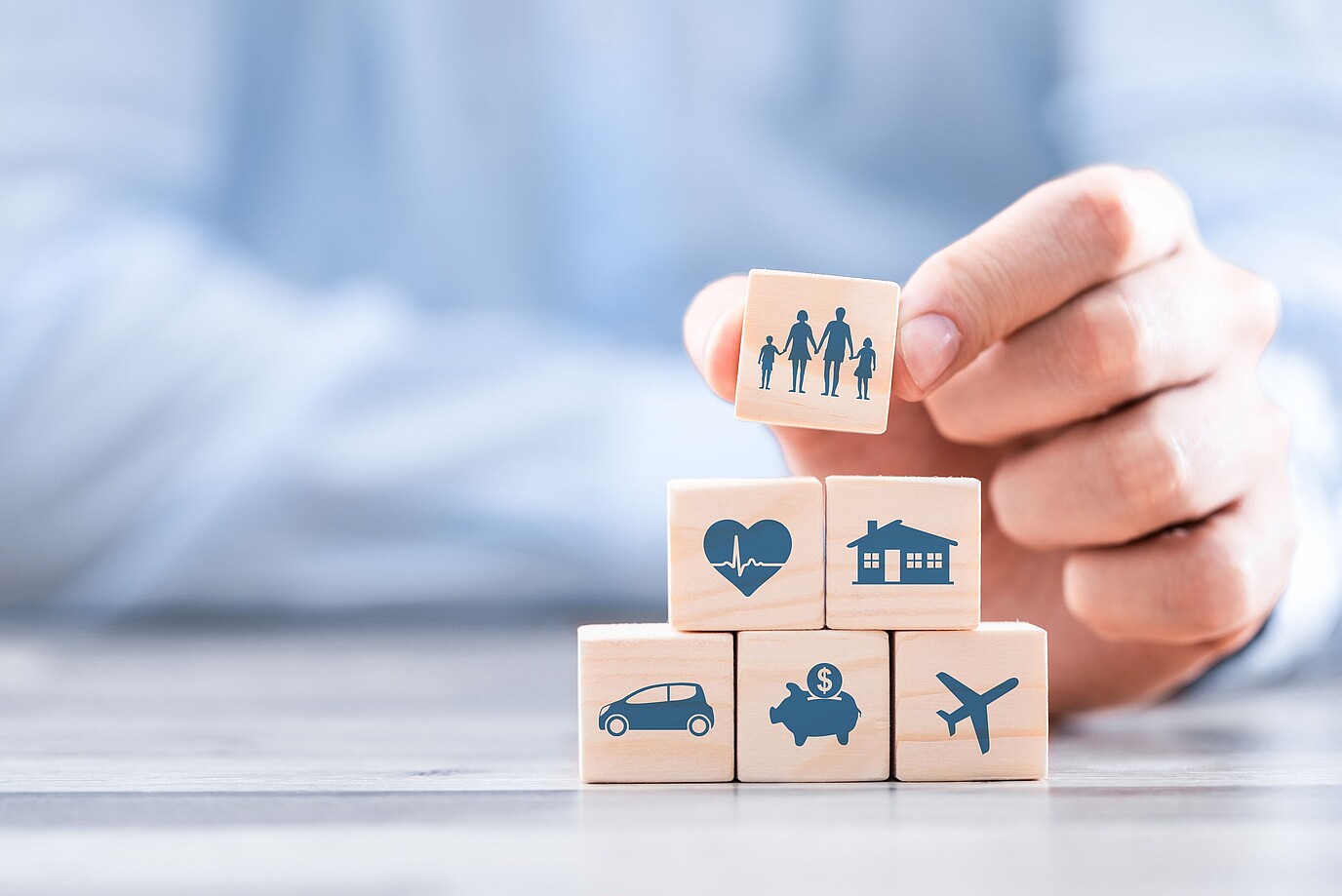 Ein Mann stapelt Holzklötze mit Symbolen für Familie, Gesundheit, Wohnen, Auto, Sparen und Reisen.