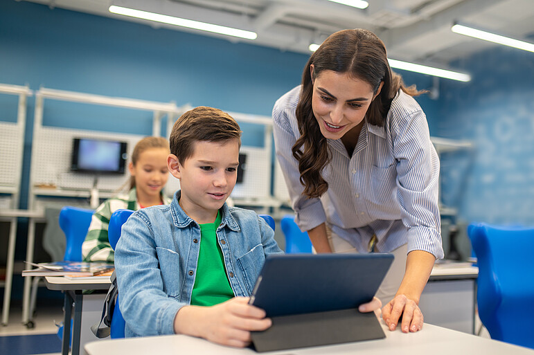 Eine Lehrerin schaut mit ihrem Schüler auf ein Tablet.