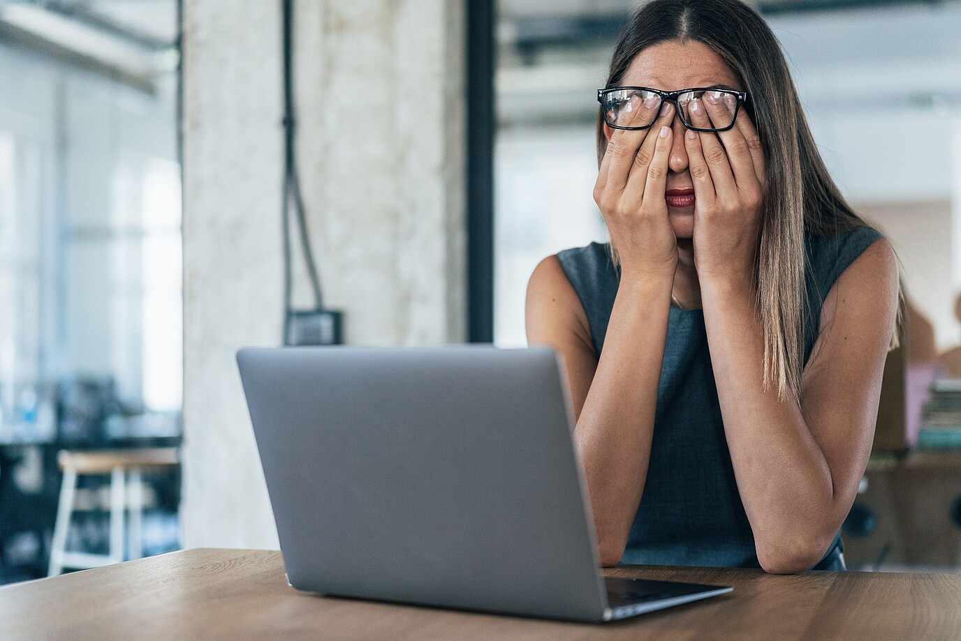 Eine Frau sitzt am Laptop und hat erschöpft ihre Hände im Gesicht.