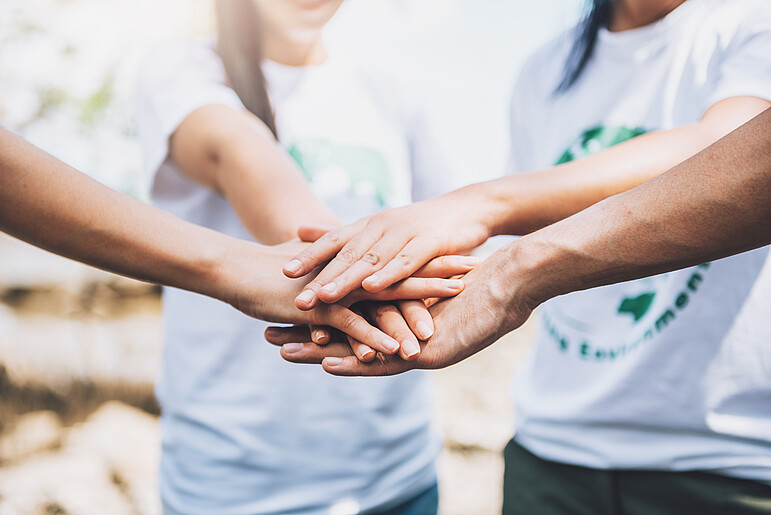 Mehrere Personen die ihre Hand im Kreis zusammenlegen um Teamwork zu symbolisieren.