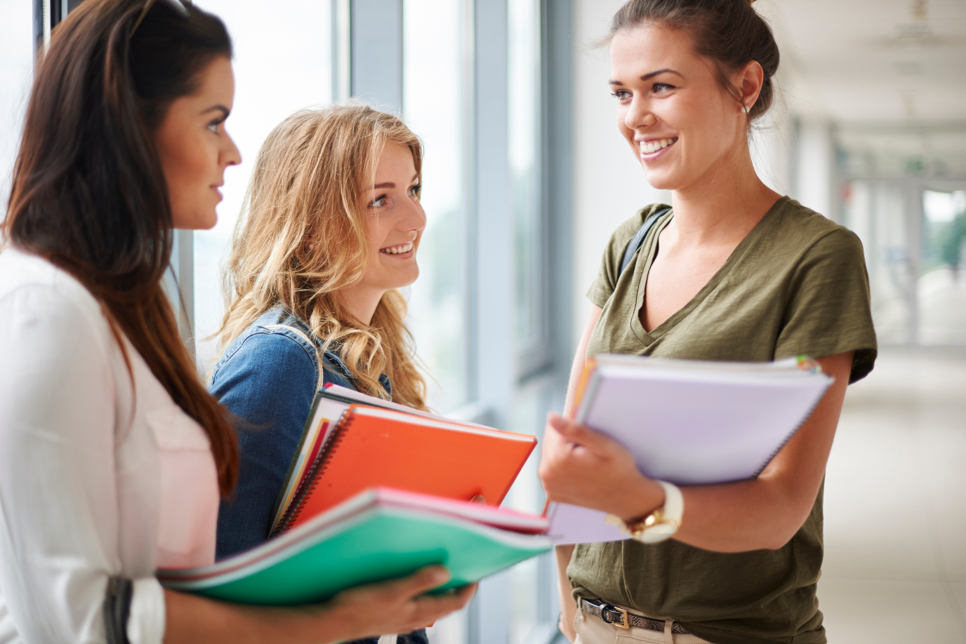 Drei jungen Frauen stehen zusammen mit Schulunterlagen in den Händen in einem Gang,