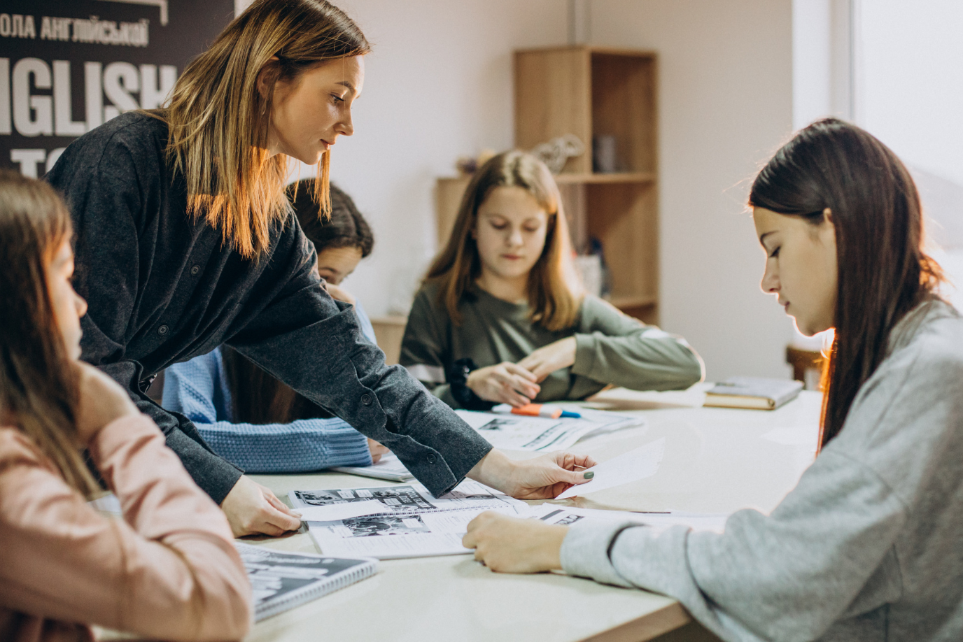 Eine Lehrerin erklärt ihren Schülerinnen den Unterricht am Tisch.